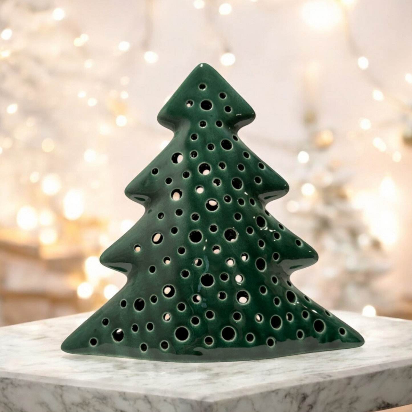 ceramic green Christmas tree shaped candle holder on a light marble table with Christmas lights in the background